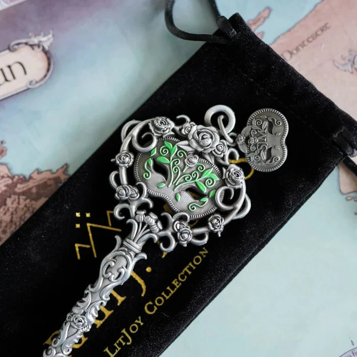 Officially licensed ACOTAR Spring Court key by Sarah J. Maas LitJoy Collection — silver rose filigree key with glowing green enamel rose bouquet centerpiece and heart-shaped charm, resting on its branded black velvet drawstring pouch against the Prythian map background